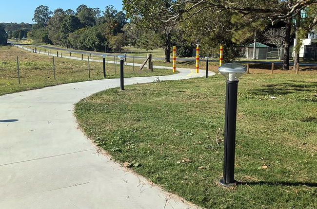 Solar bollard lights installed along curved park pathway in outdoor landscape