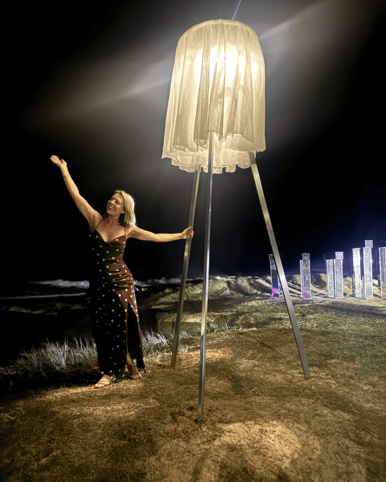 Artist Jodie Wuestewald beside the illuminated KAJI sculpture at Currumbin Beach during SWELL Sculpture Festival 2026.